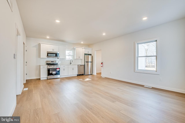 unfurnished living room with light wood-style flooring, recessed lighting, a sink, visible vents, and baseboards