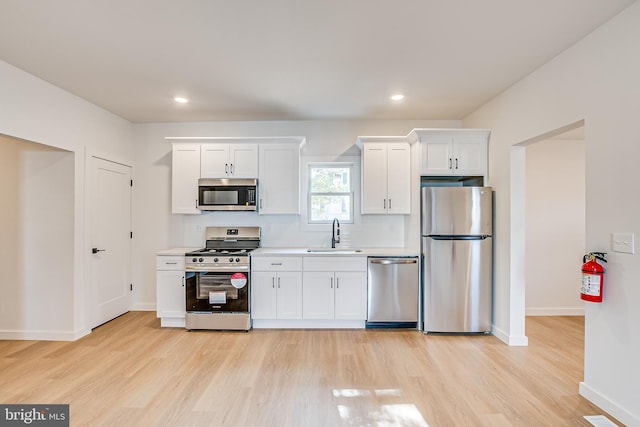 kitchen with white cabinets, stainless steel appliances, a sink, and light countertops