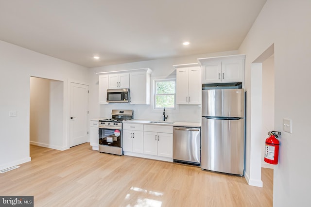 kitchen featuring a sink, white cabinetry, light wood-style floors, light countertops, and appliances with stainless steel finishes