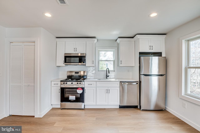 kitchen with light wood-style flooring, a sink, white cabinets, light countertops, and appliances with stainless steel finishes