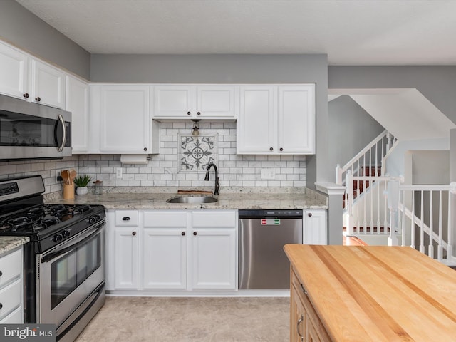 kitchen featuring a sink, light stone counters, appliances with stainless steel finishes, and white cabinets