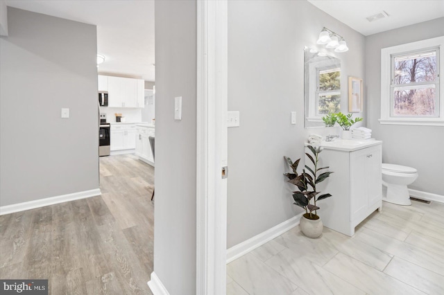 bathroom with visible vents, toilet, vanity, wood finished floors, and baseboards