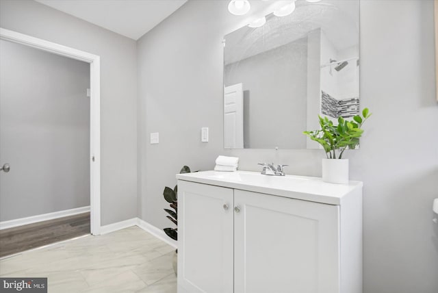 full bath featuring marble finish floor, baseboards, walk in shower, and vanity