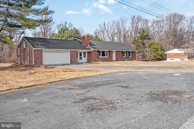 ranch-style home featuring a garage, a chimney, aphalt driveway, and brick siding