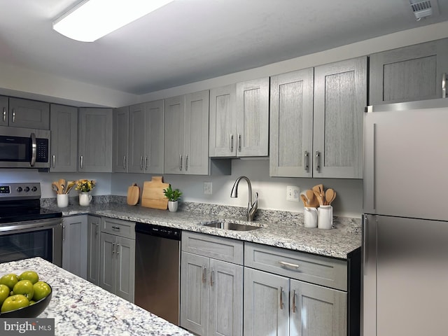 kitchen featuring visible vents, light stone countertops, stainless steel appliances, gray cabinetry, and a sink