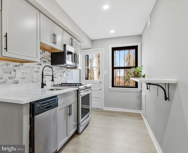 kitchen featuring backsplash, light wood-style flooring, appliances with stainless steel finishes, a sink, and baseboards