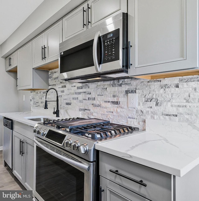 kitchen with light stone counters, appliances with stainless steel finishes, backsplash, gray cabinets, and a sink