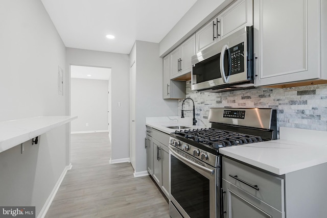 kitchen with tasteful backsplash, gray cabinets, appliances with stainless steel finishes, a sink, and baseboards