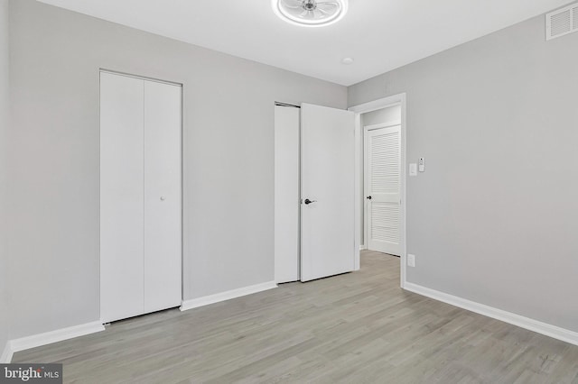 unfurnished bedroom with light wood-type flooring, visible vents, baseboards, and two closets