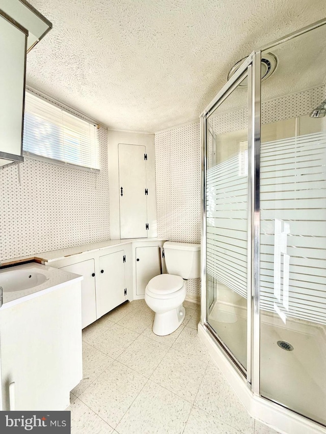 bathroom featuring toilet, a stall shower, a textured ceiling, wallpapered walls, and vanity