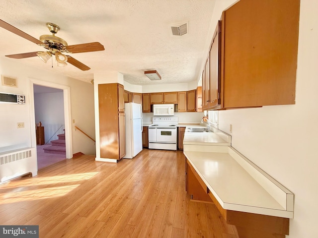 kitchen with visible vents, light wood-style flooring, radiator heating unit, white appliances, and brown cabinetry