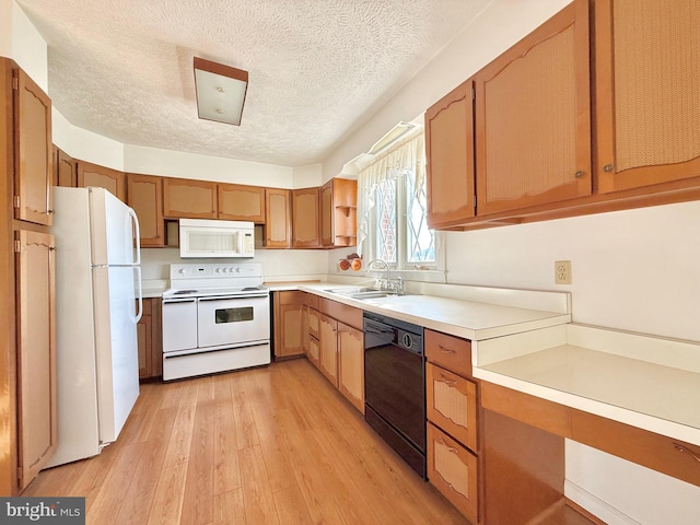 kitchen with light wood finished floors, light countertops, white appliances, a textured ceiling, and a sink