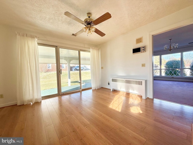 empty room featuring radiator heating unit, wood finished floors, visible vents, and a textured ceiling