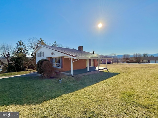 view of side of home featuring brick siding, a lawn, a chimney, and metal roof