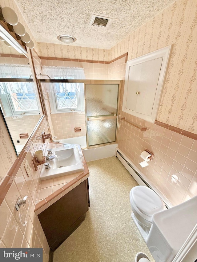 bathroom with visible vents, wallpapered walls, a baseboard heating unit, tile walls, and a textured ceiling