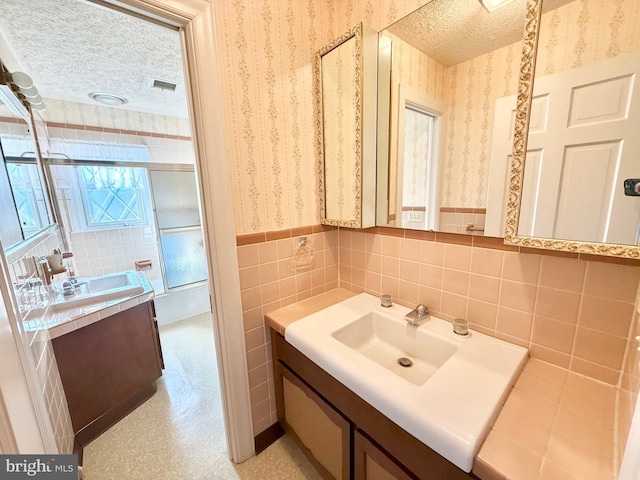 bathroom featuring visible vents, wallpapered walls, tile walls, a wainscoted wall, and a textured ceiling