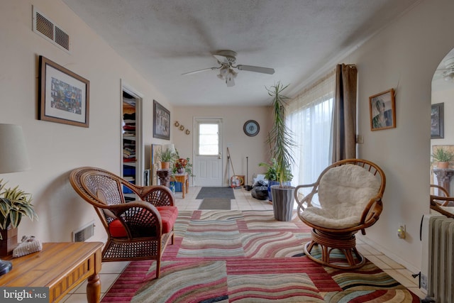 living area featuring a ceiling fan, visible vents, radiator heating unit, a textured ceiling, and tile patterned floors