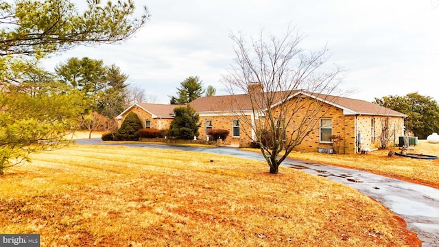 ranch-style home featuring brick siding, aphalt driveway, a front yard, central AC unit, and a chimney