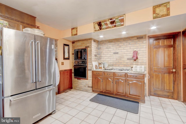 kitchen featuring a wainscoted wall, brown cabinets, black appliances, brick wall, and light tile patterned floors