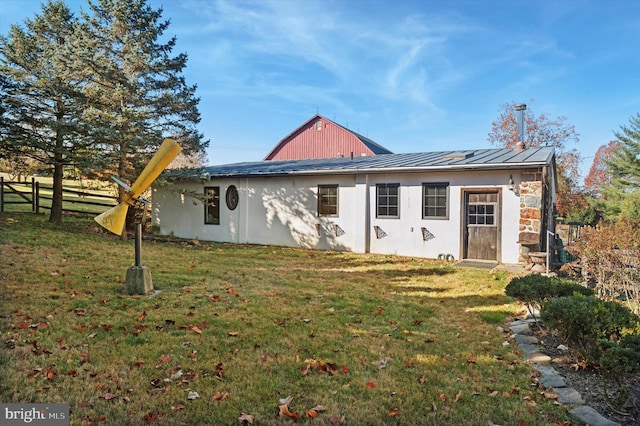 back of property with metal roof, fence, stone siding, a lawn, and a standing seam roof