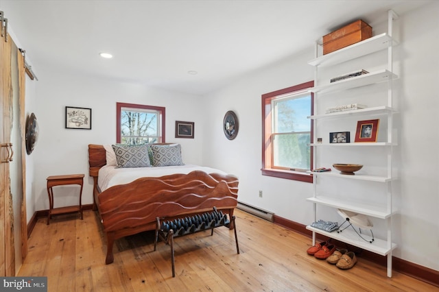 bedroom with light wood-style floors, a baseboard radiator, multiple windows, and a barn door