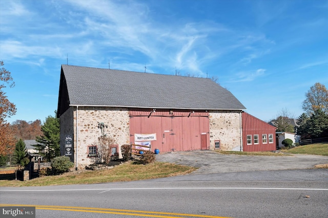 view of property exterior featuring a barn, a shingled roof, a detached garage, and an outdoor structure