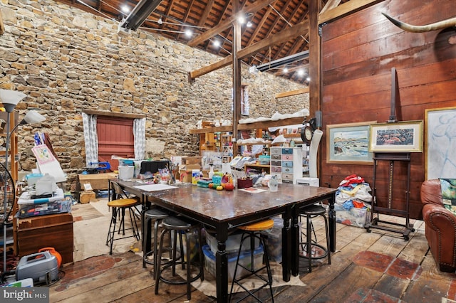 dining space with wooden walls, wood ceiling, a towering ceiling, beamed ceiling, and wood-type flooring