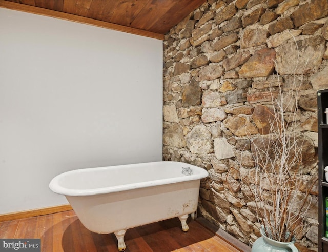 bathroom with wood finished floors, wooden ceiling, a freestanding tub, and baseboards