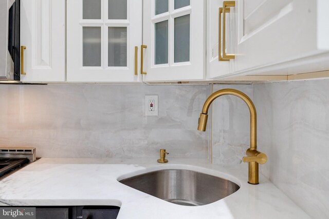 interior details featuring glass insert cabinets, tasteful backsplash, white cabinetry, and a sink