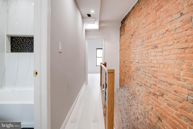 hallway featuring visible vents, baseboards, brick wall, wood finished floors, and an upstairs landing