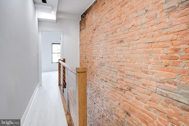 corridor with brick wall, baseboards, wood finished floors, and an upstairs landing