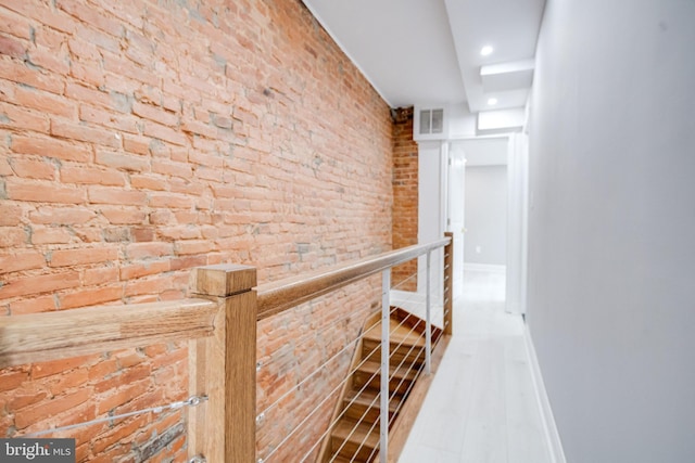 hallway with wood finished floors, visible vents, an upstairs landing, brick wall, and baseboards