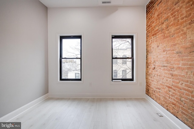 spare room with light wood-type flooring, baseboards, visible vents, and brick wall