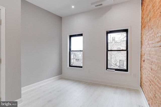 unfurnished room with recessed lighting, visible vents, light wood-style floors, brick wall, and baseboards