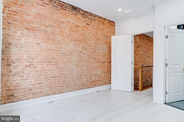 spare room featuring brick wall, baseboards, and wood finished floors