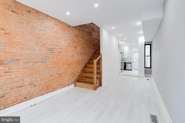 unfurnished living room featuring visible vents, stairway, brick wall, wood finished floors, and baseboards