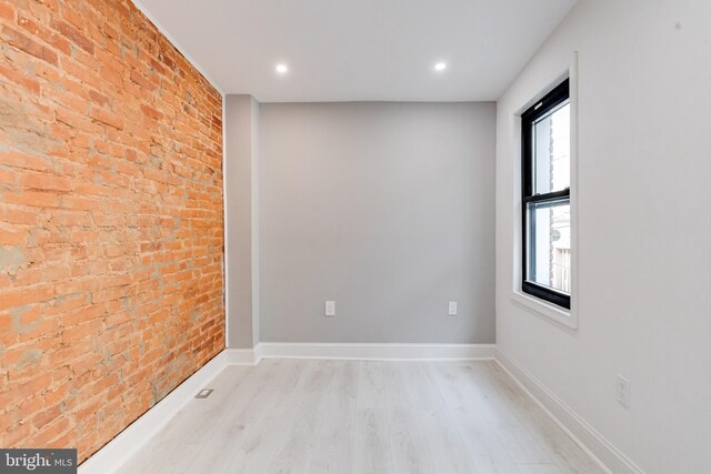 empty room featuring light wood-type flooring, brick wall, baseboards, and recessed lighting