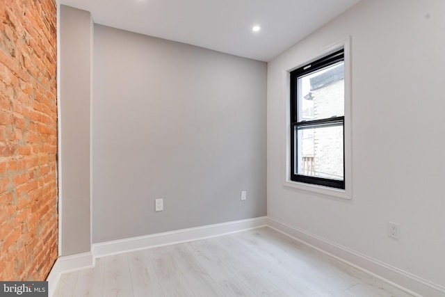 empty room with brick wall, baseboards, light wood-style flooring, and recessed lighting