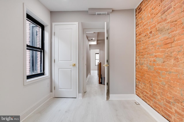 hallway featuring baseboards, brick wall, and wood finished floors