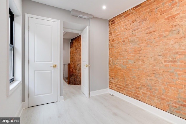 empty room featuring brick wall, baseboards, and light wood-style flooring