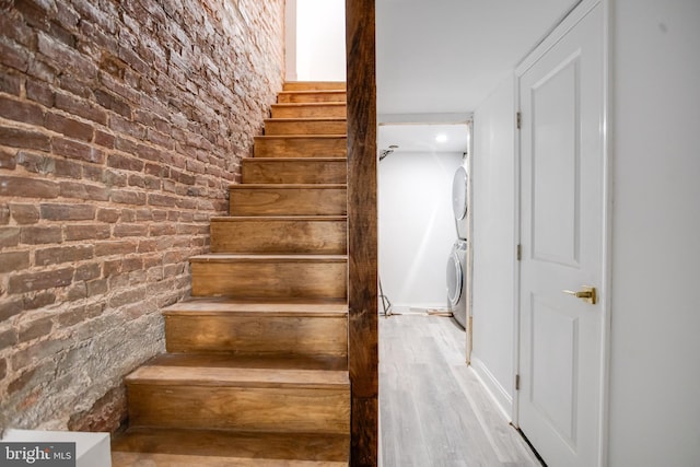 stairs with brick wall, stacked washer / dryer, and wood finished floors