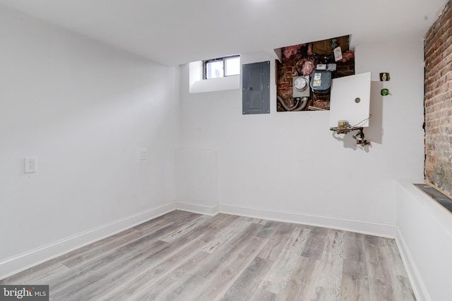 basement with light wood-type flooring, electric panel, and baseboards