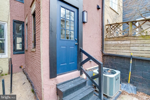 view of exterior entry with stucco siding and central air condition unit