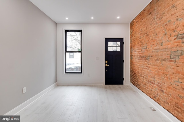 foyer entrance featuring baseboards, a healthy amount of sunlight, light wood finished floors, and brick wall