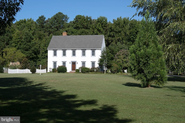 colonial-style house featuring a front lawn, a chimney, and fence