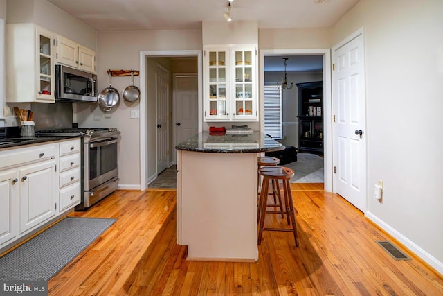 kitchen featuring visible vents, glass insert cabinets, appliances with stainless steel finishes, light wood-style floors, and a kitchen bar