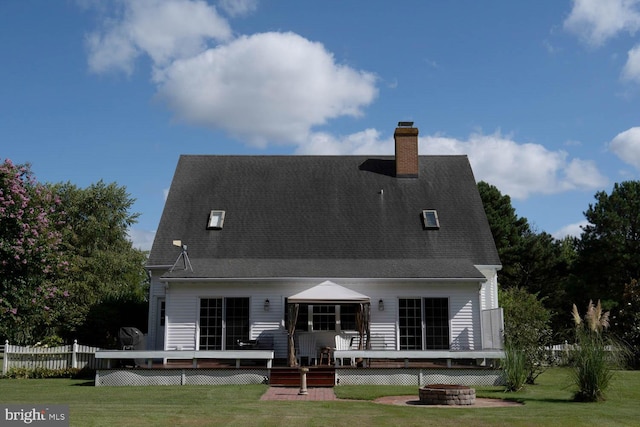 back of property with a deck, a chimney, a lawn, and a fire pit