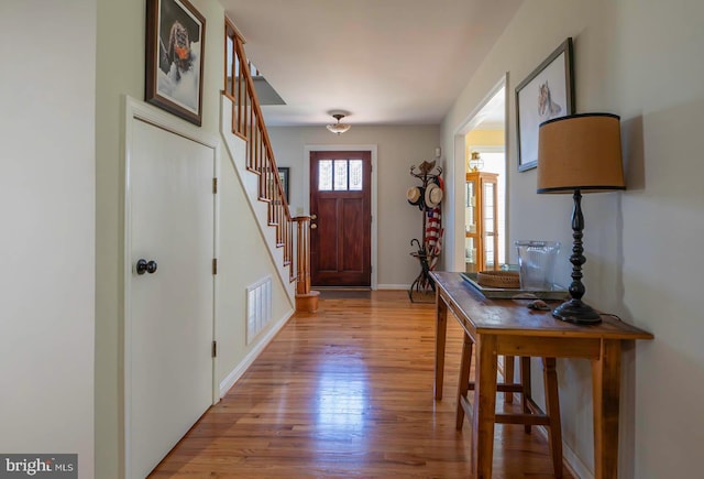 entryway with wood finished floors, visible vents, baseboards, and stairs