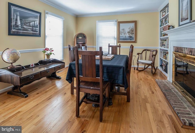 dining area featuring crown molding, light wood-style floors, a healthy amount of sunlight, and a fireplace