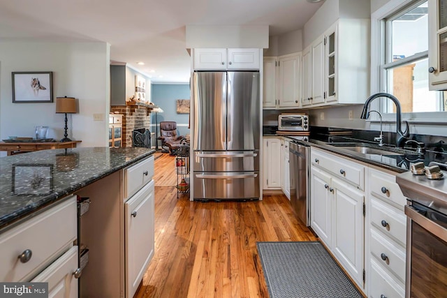 kitchen with light wood-type flooring, a fireplace, stainless steel appliances, and a sink